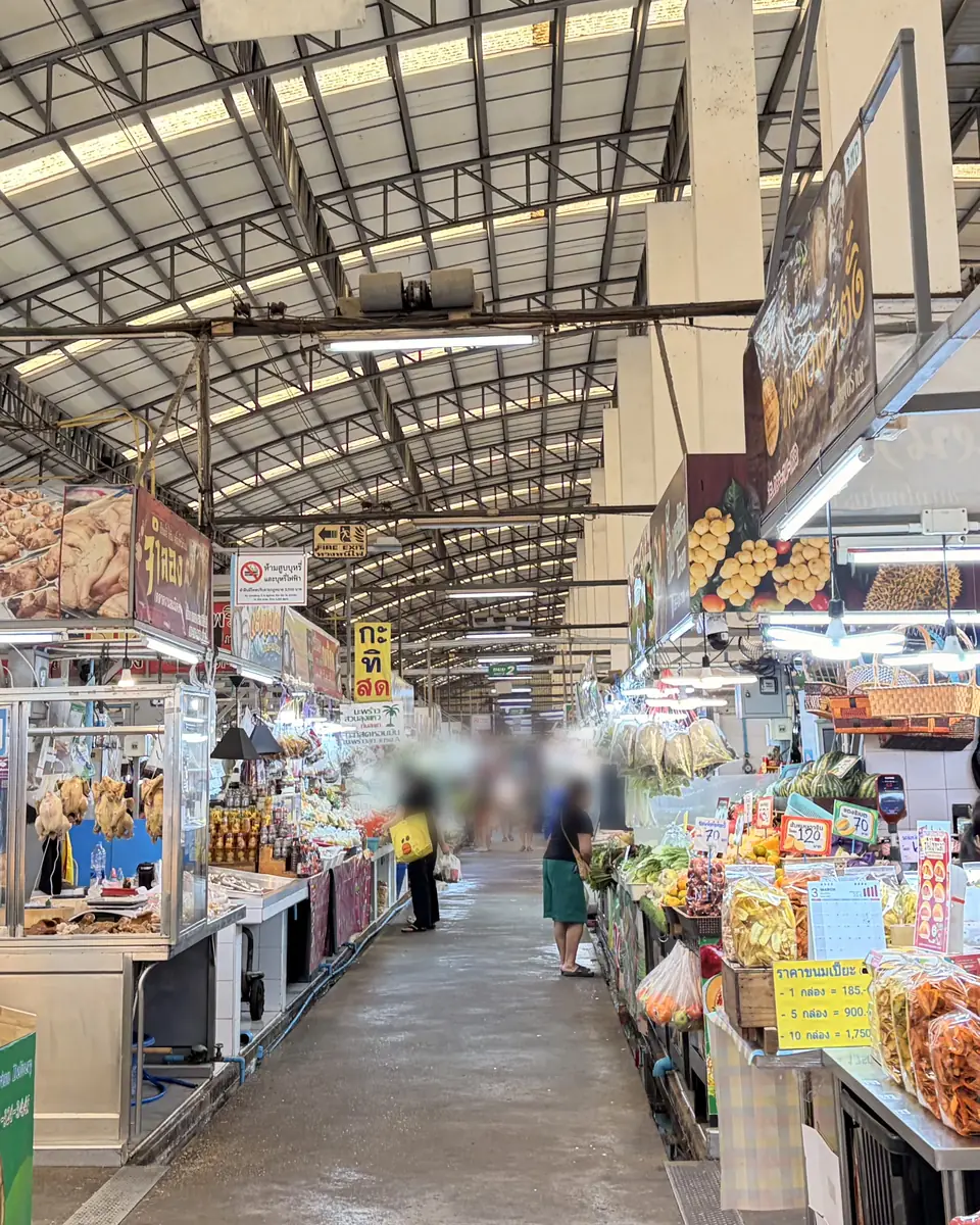 A covered market aisle lined with fruit, snack and food stalls, with shoppers walking between them