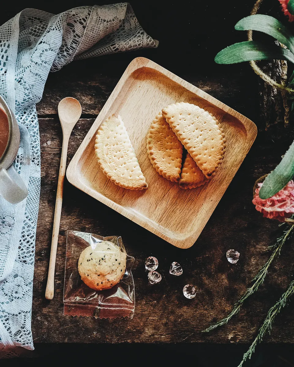 A cup of hot chocolate and wrapped cookies on a wooden tray, on a dark table with a lace cloth.